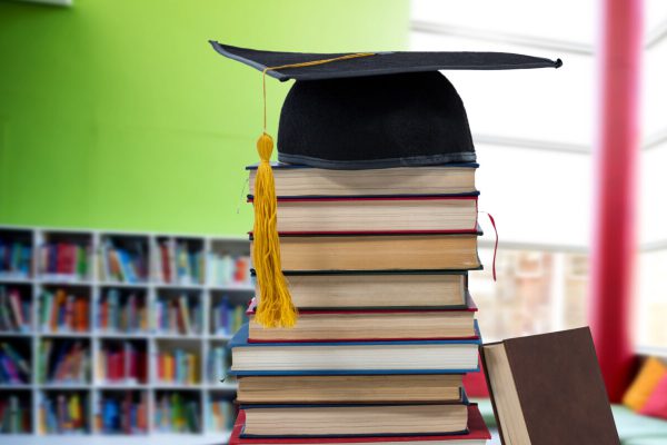 Digital composite of Books and graduation hat in education library