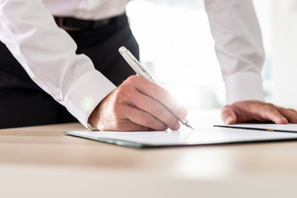 Business executive signing a contract with ink pen with bright sunlight in background.