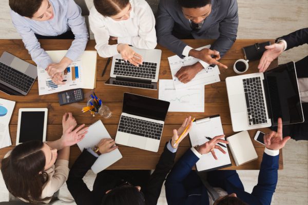 Business meeting. Busy people work in office, top view on wooden table with mobile phones, laptop, tablet and documents papers with diagram, corporate background